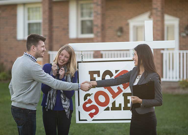 couple-shaking-hands-with-realtor-in-front-of-sold-home