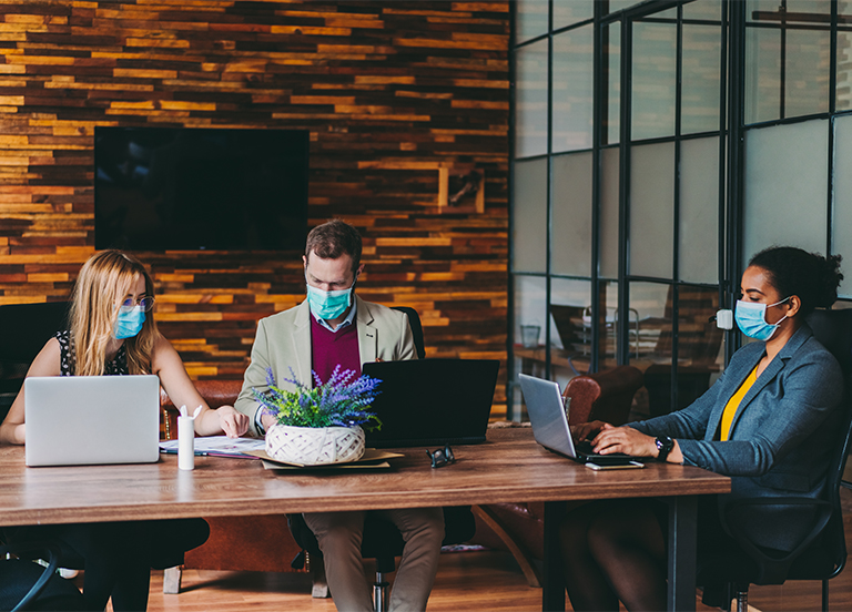 business people wearing masks sitting at a table