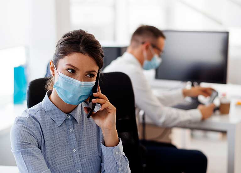 man and woman wearing masks at their desks in the office