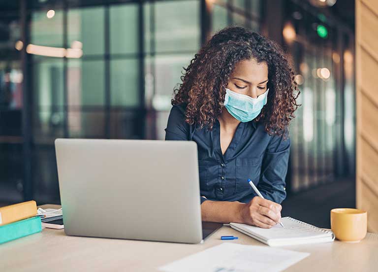 Mulher escrevendo no papel no escritório usando máscara