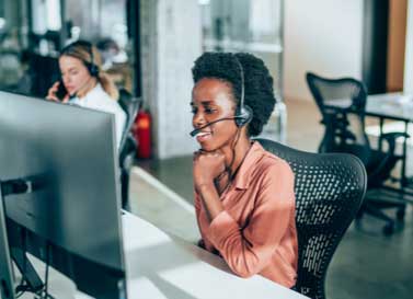 Two-female-support-sitting-behind-computers-at-desks-use-headsets-to-speak-to-customers.